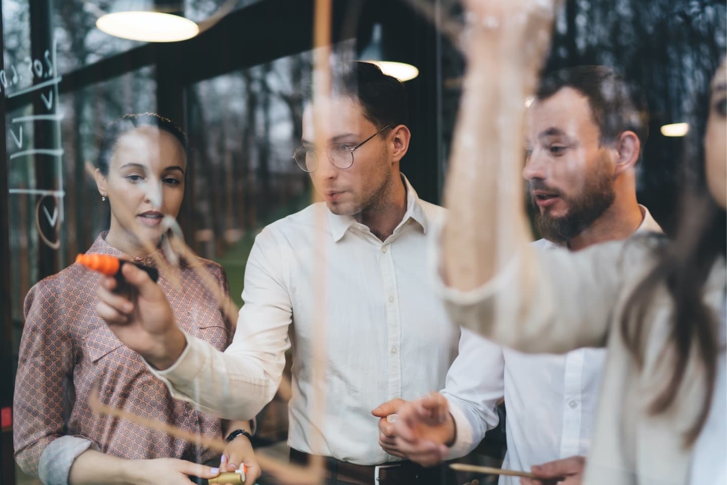 Three colleagues collaborating at a glass board, with one person writing notes using an orange marker.