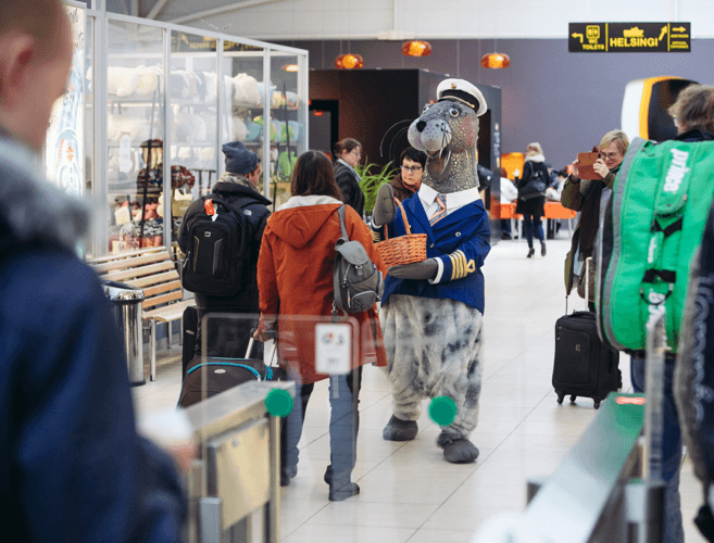 Person in seal captain costume greeting travellers in Helsinki airport terminal with a basket.