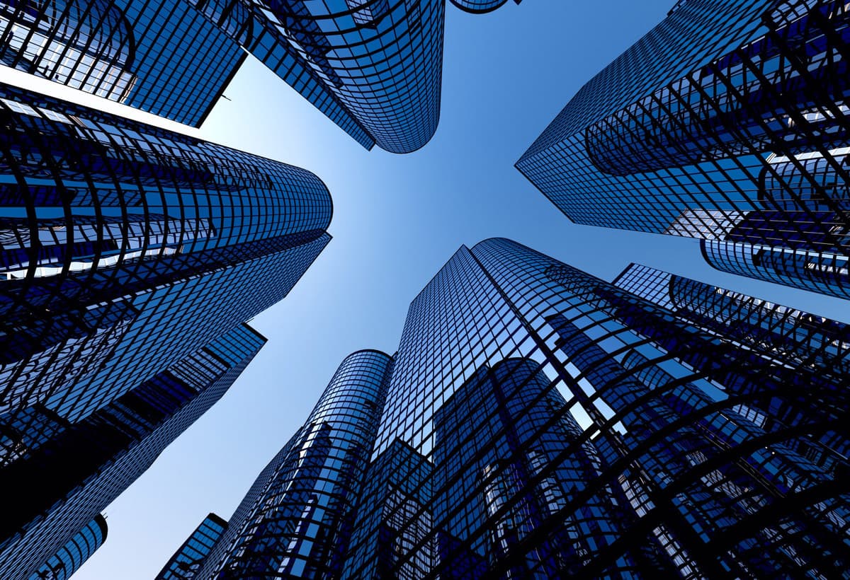 Looking up at modern glass skyscrapers against a clear blue sky, creating a dramatic architectural perspective.