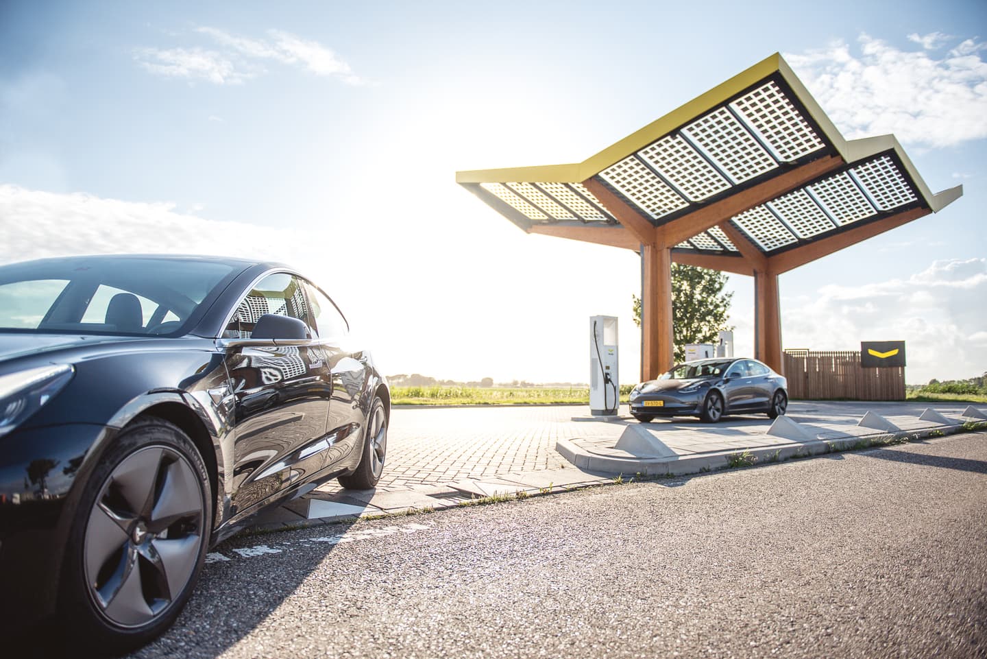 Electric vehicles charging at a modern solar-powered station with wooden canopy structure under blue sky.