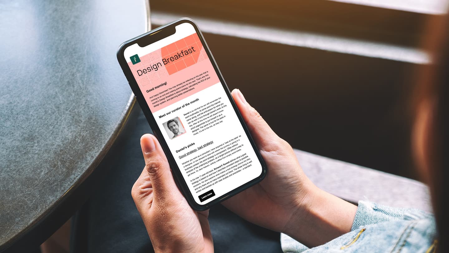 Hands holding smartphone displaying "Design Breakfast" newsletter with coral header, curator profile and article sections.